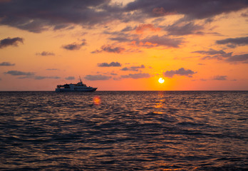 Fototapeta na wymiar Orange sunset over the sea with a passing ship