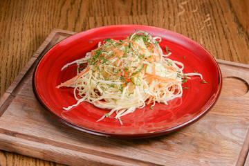 Sauerkraut. Sour cabbage salad served on red plate over dark rustic wooden table background