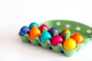 Colorful eggs in the open carton box on white background. Easter holiday concept with copy space.