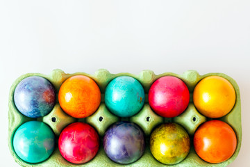 Top view of colorful eggs in the carton box on white background. Easter holiday concept with copy space.