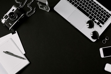 Framed mockup for business and freelance concept. Stylish workspace of designer with laptop, vintage film camera, notebook, headphones, pen and smartphone on black desk. Flat lay, top view