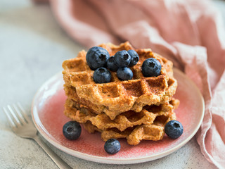 Easy healthy gluten free oat waffles with copy space. Stack of appetizing homemade waffles with oat flour decorated blueberries, on plate over light gray cement background