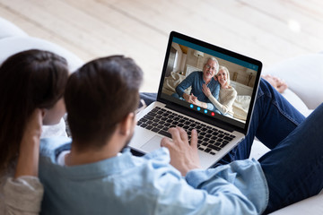 Couple communicating with elderly parents living abroad using computer and videocall application, laptop screen view over spouse shoulder. Distant virtual communication modern technology usage concept - obrazy, fototapety, plakaty