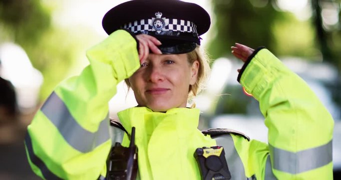 4K Close up portrait of policewoman on patrol, putting on hat & smiling at camera. Slow motion.