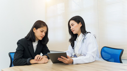 Young Asian female doctor gives consultation and listen to adult female patient’s symptoms in office. Patient having consultation with doctor in office. Medical and healthcare concept.