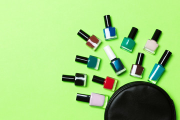 Top view of the set of nail polishes and bright gel varnishes fallen out of cosmetics bag with copy space on green background. Trendy nail concept