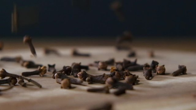 Dry cloves falling on dark rustic wooden table over black background in slowmotion. Spicy food ingredient.