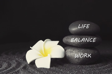 Work-life balance concept. Stacked stones and plumeria flower on sand