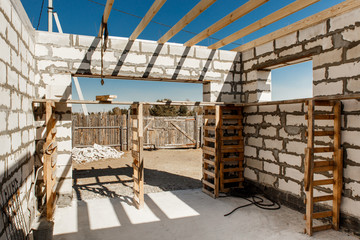 Building site of a house under construction. Unfinished house walls made from white aerated autoclaved concrete blocks. Scaffolding for workers assembled from boards and Euro-pallets.