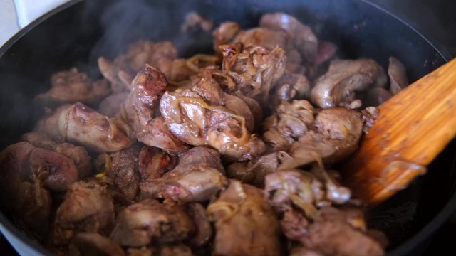 chicken liver with onion fried in the pan with a wooden kitchen spatula