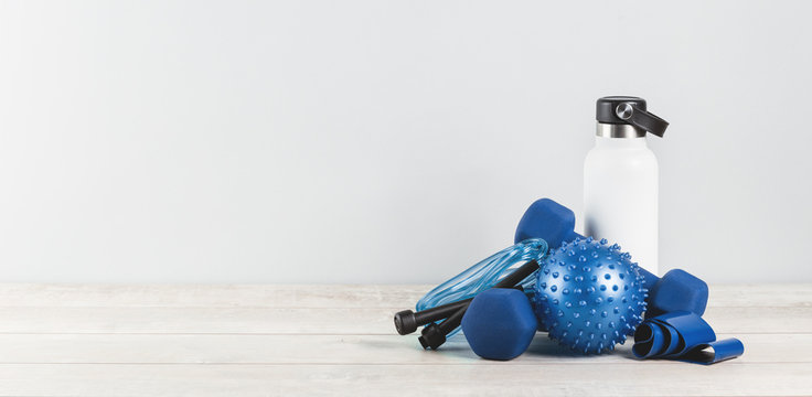 Healthy lifestyle blue gender neutral sports accessories grouped around white water bottle flask on white grey wood. Fitness and exercise monochrome items banner with copy space - Powered by Adobe