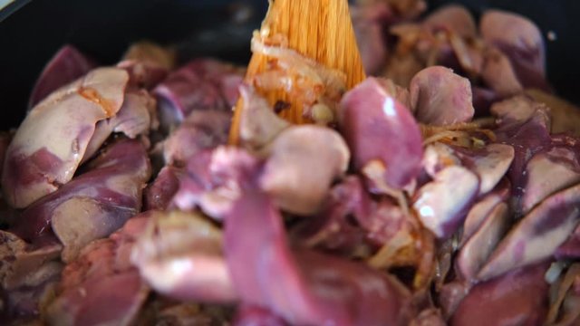 chicken liver with onions fried in the pan with a wooden kitchen spatula
