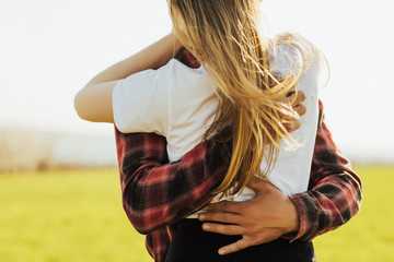 Cropped shot of young man embracing her  girlfriend from the back at the green field background.  Happiness couple concept. Romantic and togetherness in spring day. Love, trust, romance.