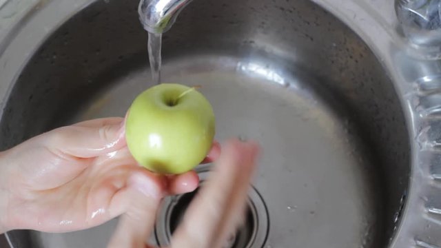 man washes an apple with soap and a brush in the sink