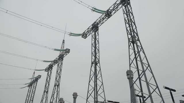 Metal structures and electrical insulators at a high voltage substation against the sky. Low angle shooting. Power wires with high voltage. Slow and smooth camera movement.