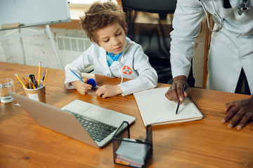 Caucasian teenboy as a doctor consulting for patient, giving recommendation, treating. Little doctor during working with older colleague. Concept of childhood, human emotions, health, medicine.