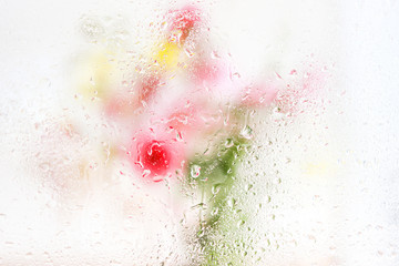 close up of a window with rain drops on it, thought which we can see a blured flower bouquet
