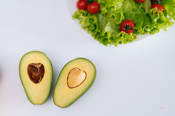 Fresh ripe sliced avocado cut in half on white table, salad leaves in the background. Concept of...