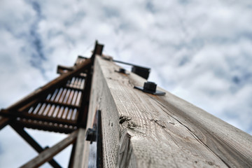 Bright photo looking up a tall industrial wooden structure towards the sky with a backdrop of fluffy clouds