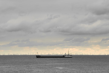 Fototapeta premium An industrial view of a cargo ship with modern wind turbines in the background under a dramatic sky