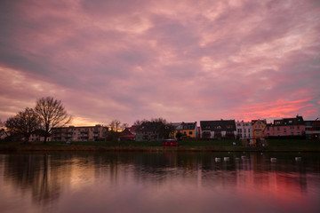 Naklejka premium Epic sunset light casts over a calm German Lake with traditional houses in the background and birds on the water