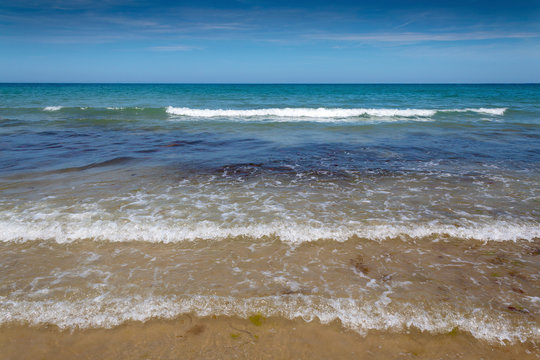 Waves rolling onto a sandy beach on a hot summer day with a blue sky and light clouds