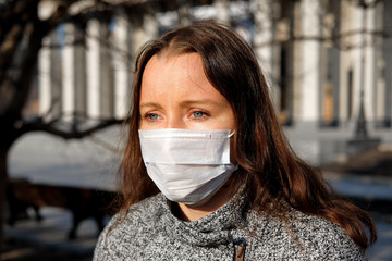 A woman in a medical mask walks alone on the street during the quarantine. Portrait of a female in a protective face mask against coronavirus.