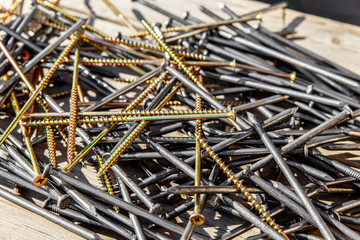 Iron nails and screws on a wooden background. Long, metal, carpenter's nails and self-tapping screws for construction. Fixing tool. The view from the top.
