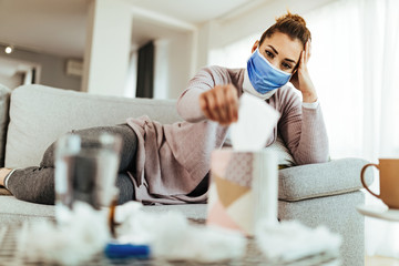 Woman wearing face mask while sitting on the sofa and taking a tissue for the box.