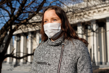 A woman in a medical mask walks alone on the street during the quarantine. Portrait of a female in a protective face mask against coronavirus.
