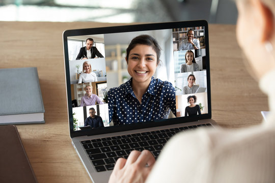 Laptop screen over woman shoulder view, indian businesswoman leading videoconference distant communication group videocall conversation. Diverse friends using modern tech enjoy virtual meeting concept - Powered by Adobe