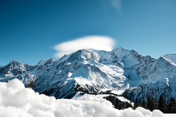 Alpine landscape with adiabatically cooled clouds formed at the peak of the mountain and snowy foreground interest