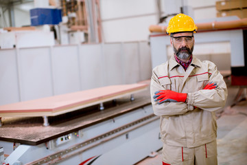Confident mature man standing with crossed arms in the factory manufacturing unit with orange helmet
