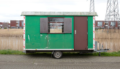 Old green wooden trailer on wheels stands at the side of the road