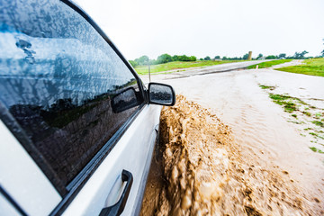 a white-black car rides on a road in a deep mud puddle and makes the front wheel splashes in the...