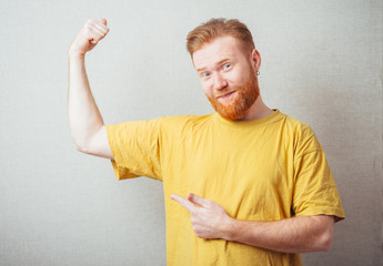 on a gray background man with a beard in the yellow shirt is outraged and shows forefingers biceps