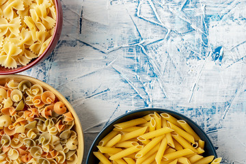 ceramic bowls of different colors with different pastas on a white and blue textured background