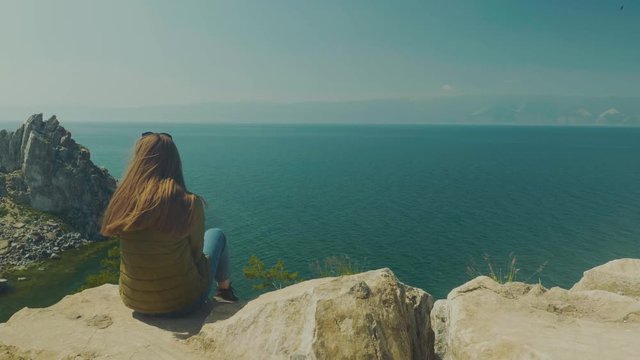 Girl on the shore of lake Baikal. Looks into the distance. sits. Shamanka Bay. Olkhon Island, Russia, Siberia. UNESCO world heritage site