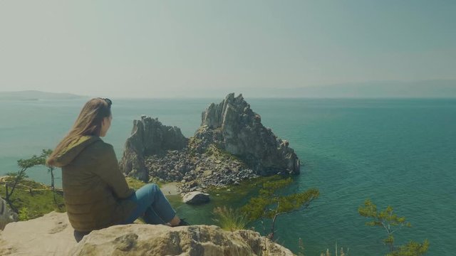Girl on the shore of lake Baikal. Looks into the distance. sits. Shamanka Bay. Olkhon Island, Russia, Siberia. UNESCO world heritage site