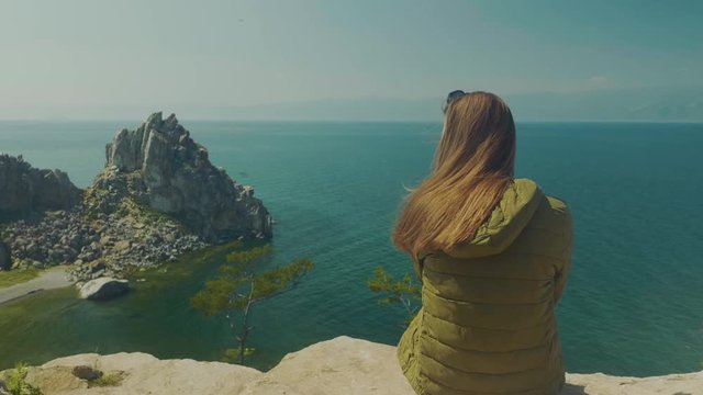 Girl on the shore of lake Baikal. Looks into the distance. sits. Hair in the wind. The Cliff Bay Is A Shaman. Olkhon Island, Russia, Siberia. UNESCO world heritage site