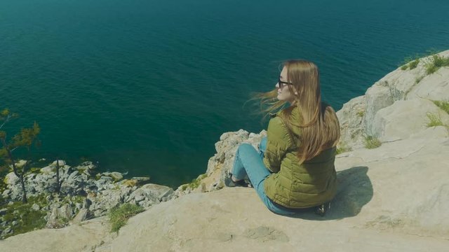 Girl on the shore of lake Baikal. Looks into the distance. sits. Shamanka Bay. Olkhon Island, Russia, Siberia. UNESCO world heritage site