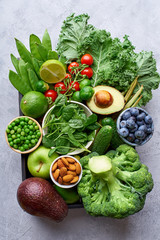 Creative flat lay with healthy vegetarian meal ingredients. Raw food concept. A variety of organic fruits, nuts, berries and vegetables in wooden box on concrete background