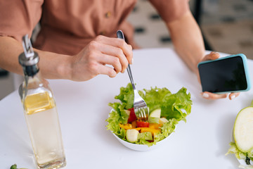 Close-up of women's hands mix fresh vegetable salad in salad bowl using fork. Cooking of vegetarian salad in kitchen with modern interior. Concept of healthy eating.