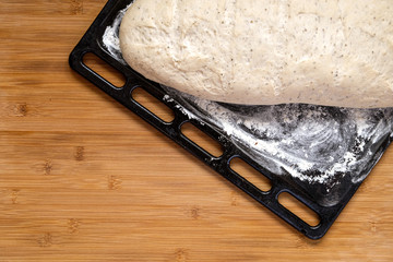 Raw dough for bread ready to bake on a black baking tin and a wooden board.