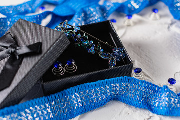 Beautiful brooch with blue and aquamarine stones and rhinestones of different sizes, metal base pins in a gift box with a black bow, around the ribbon with silver threads and springs.