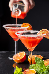 Top view of blood orange cocktail glasses with woman's hand serving, selective focus, and black background, vertical