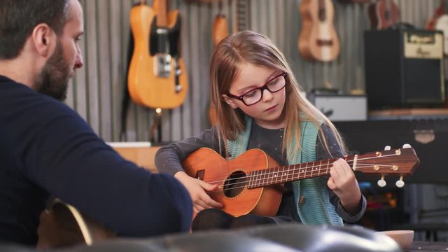 Dad teaching guitar and ukulele to his daughter.Little girl learning guitar at home.Close up.Ukulele class at home. Child learning guitar from her father