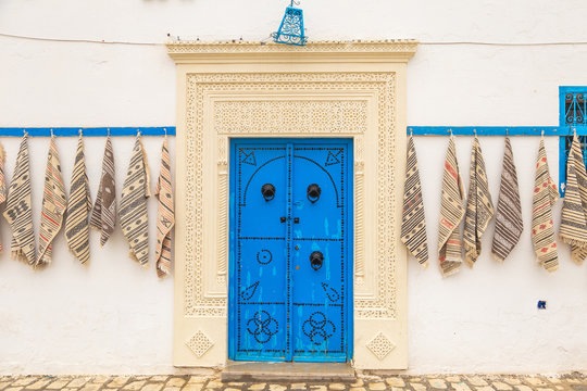 Narrow streets of old city in Tunisia country. Walls of old building and blue wooden doors with decorative elements. Traditional small carpets selling in streets of Tunisia.