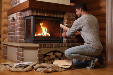 Man putting dry firewood into fireplace at home. Winter vacation - obrazy, fototapety, plakaty