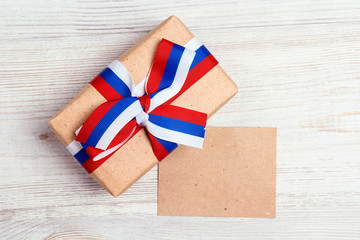 Fototapeta premium Gift box with Russian flag color ribbon on light wooden background and blank paper card.